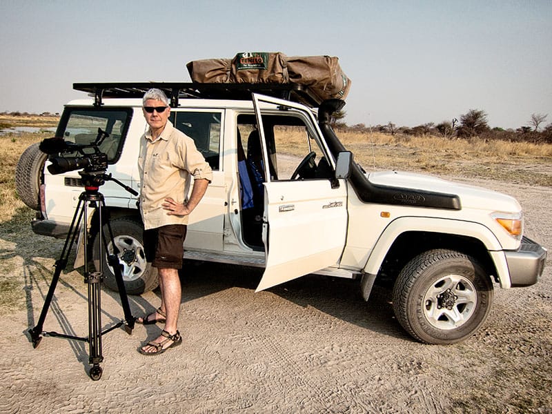 Michael Marx steht mit Kamera vor einem Allrad-Jeep mit Dachzelt